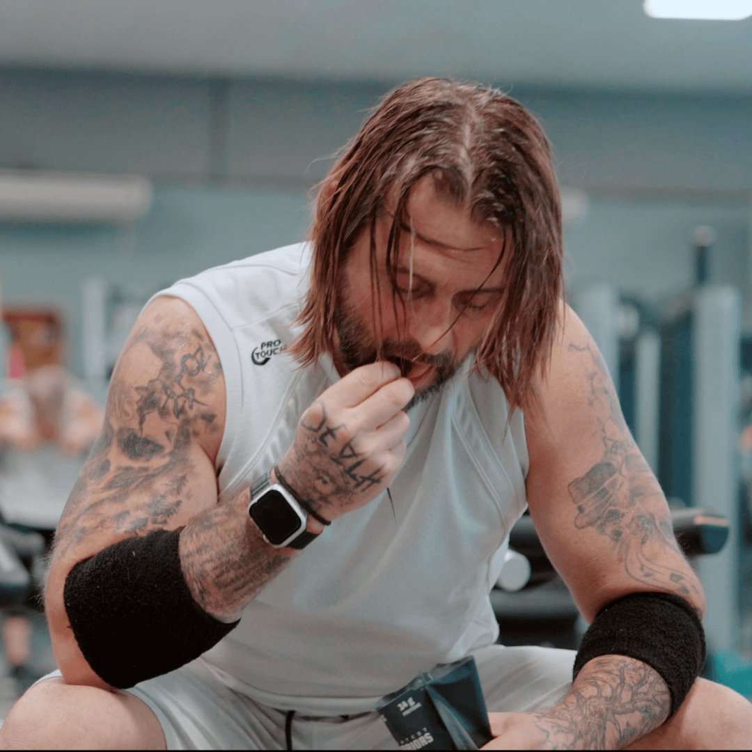 Homme tatoué mangeant de la viande séchée à la salle de sport, illustrant une collation riche en protéines idéale pour les entraînements et la récupération musculaire.